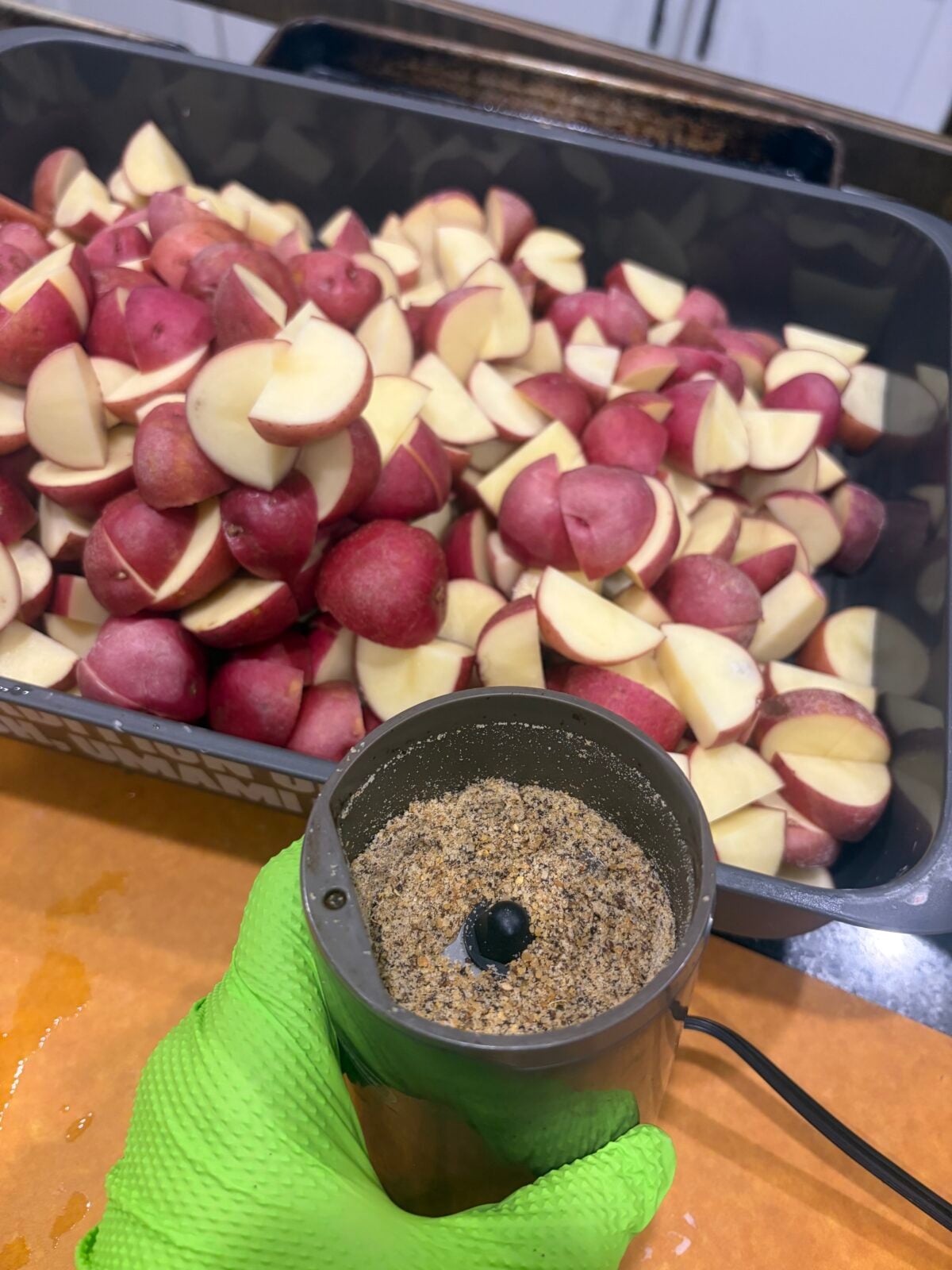 Freshly ground seasoning being prepared beside a large container of quartered red potatoes.