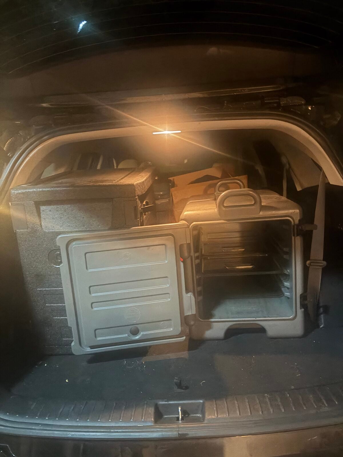 Insulated food carriers packed in the back of a vehicle for transporting hot barbecue to a cooking event.