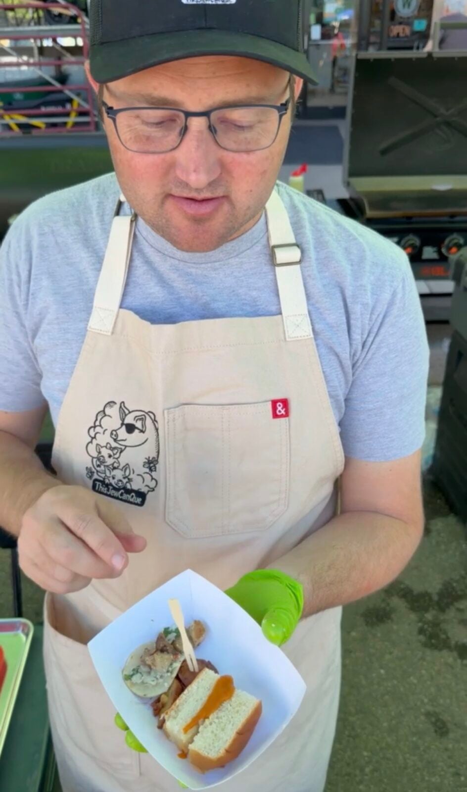 Adam from ThisJewCanQue serving a food boat with a pulled pork slider, grilled chicken taco and seasoned potato sample.