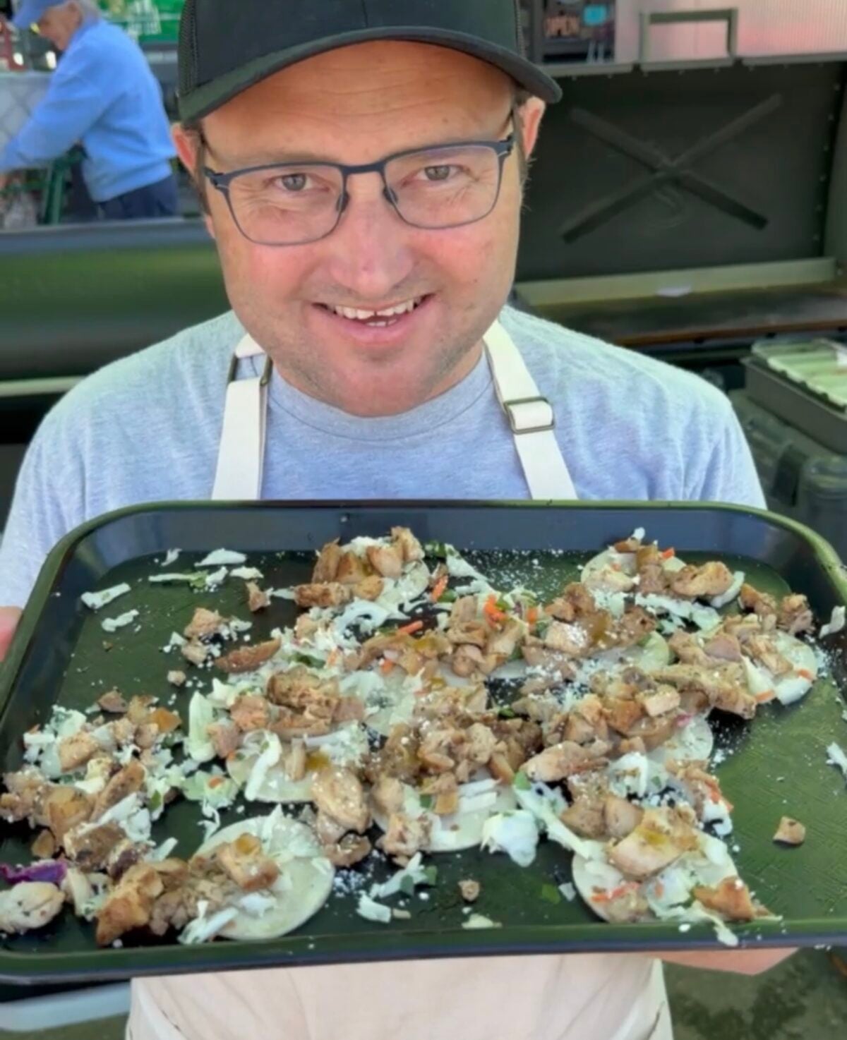 Adam from ThisJewCanQue holding a tray of mini grilled chicken tacos topped with slaw, cotija cheese and sauce.